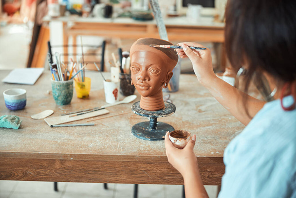 Female ceramic artist painting on clay sculpture in workshop - 写真・画像