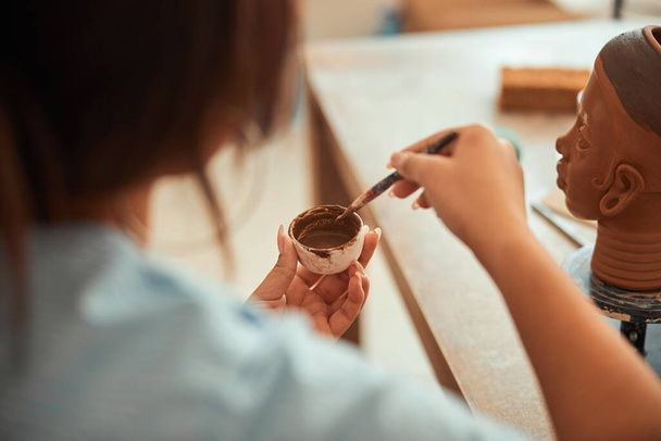 Young woman holding paintbrush and bowl with brown paint - Foto, imagen