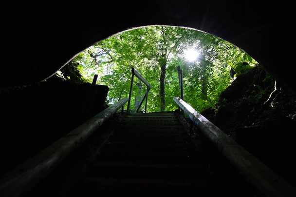 Blick aus der Höhle mit Treppe, die Sonne scheint durch die Bäume. - Foto, Bild