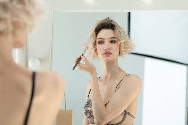 young beautiful woman stands in front of the mirror in lingerie makes make-up - Фото, зображення