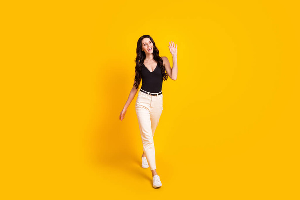 Full size photo of young attractive girl happy positive smile go walk wave hand hello hi isolated over yellow color background - Foto, afbeelding