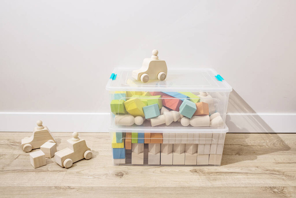 Деревянные кубики, детские игрушки, отсортированные в пластиковых контейнерах, стоят на полу в детской. Концепция создания игрушек из экологически чистых материалов, оформления дома, пошива и организации вещей.  - Фото, изображение