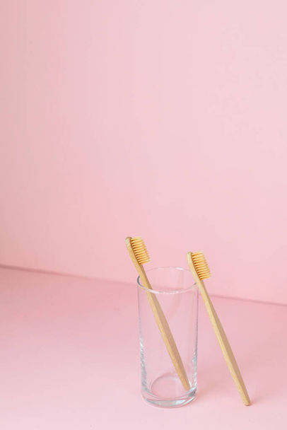 daily human hygiene, cotton swabs and cotton pads, a womans hand holding bamboo toothbrushes on a pink background in a glass or against a background of plants - Zdjęcie, obraz