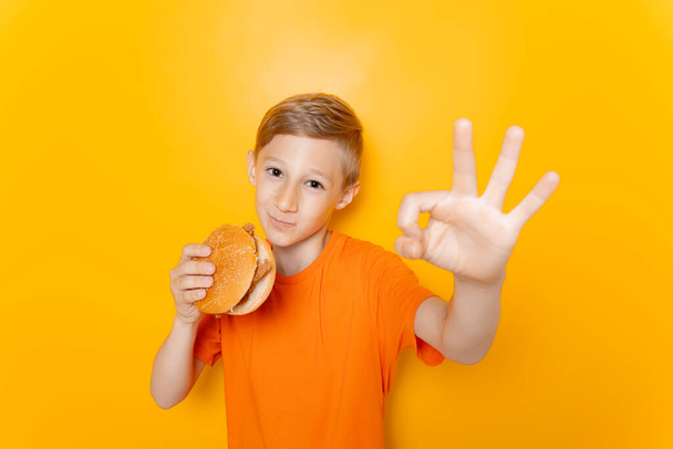 少年はハンバーガーを食べ黄色の背景でいいですね - 写真・画像