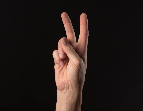 Male hand closeup gesturing peace symbol with fingers, showing V sign with arm over black background - Фото, зображення