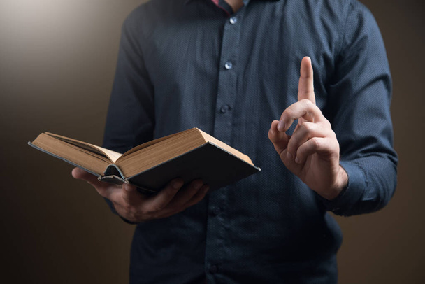 un hombre sostiene un libro y levanta su dedo índice. idea de concepto - Foto, Imagen