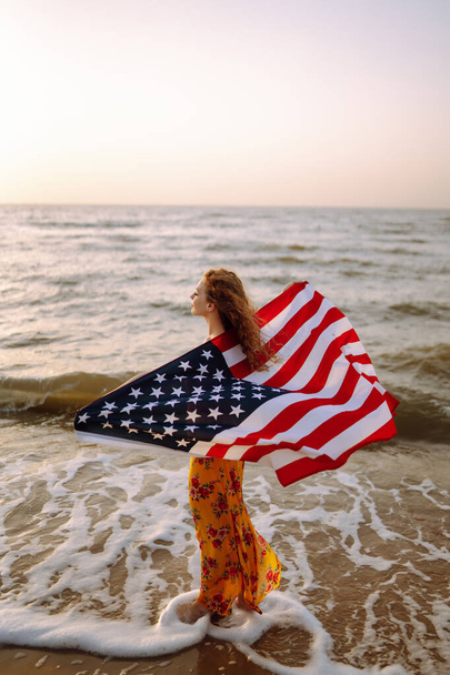 Young woman with american flag on the beach at sunset. 4th of July. Independence Day. Patriotic holiday. - Foto, afbeelding