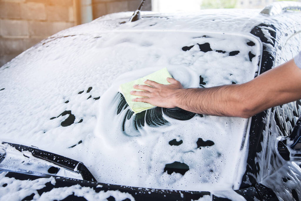 a man wipes the foam on the car with a rag. car wash - Fotoğraf, Görsel