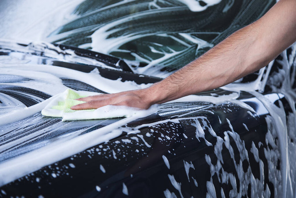 un uomo pulisce la schiuma sulla macchina con uno straccio. lavaggio auto - Foto, immagini