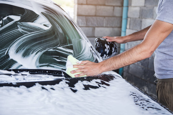 Um homem limpa a espuma do carro com um pano. lavagem de carro - Foto, Imagem
