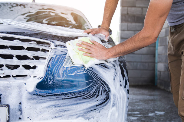 un uomo pulisce la schiuma sulla macchina con uno straccio. lavaggio auto - Foto, immagini
