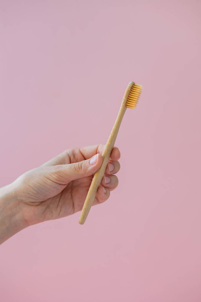 daily human hygiene, cotton swabs and cotton pads, a womans hand holding bamboo toothbrushes on a pink background in a glass or against a background of plants - Фото, зображення