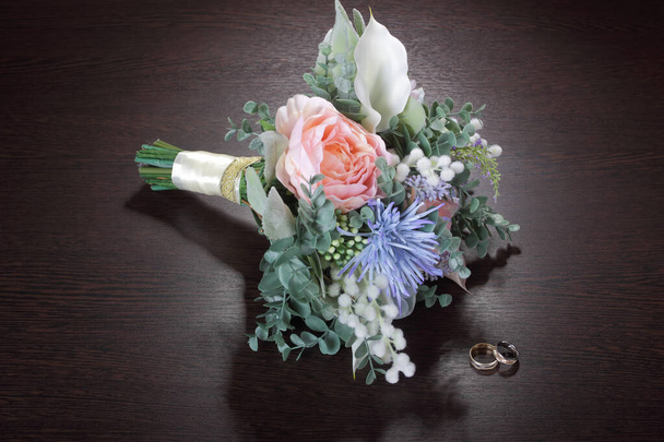 Wedding bouquet beautiful artificial flowers and wedding rings on the dark table - Foto, Imagem