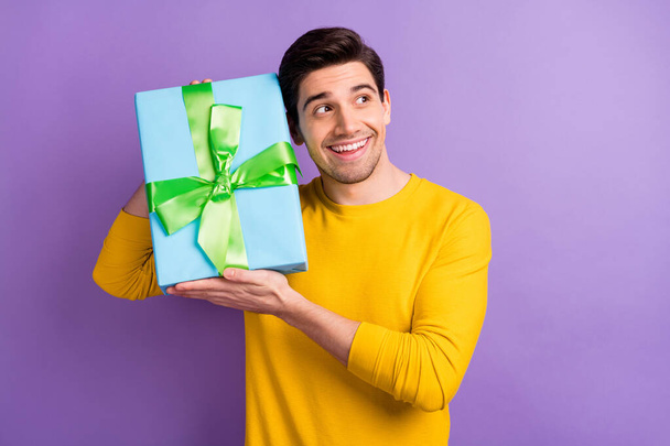 Portrait of satisfied young person hands hold giftbox near ear guessing isolated on purple color background - Фото, изображение