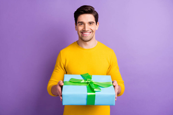 Photo of young handsome happy positive good mood smiling cheerful man give you gift box isolated on purple color background - Valokuva, kuva