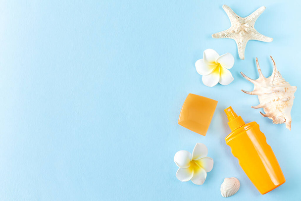 Summer sunscreen, seashells, starfish and frangipani tropical flowers on blue background top view - 写真・画像