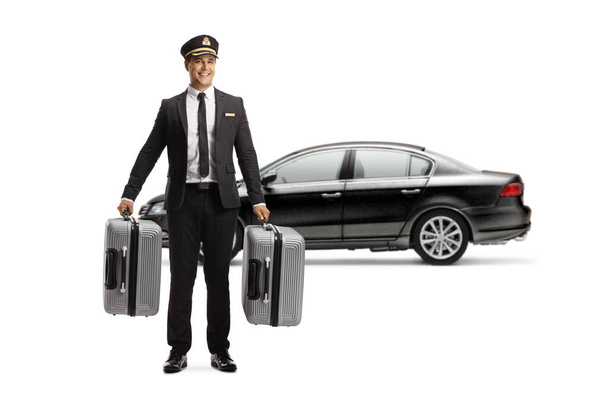 Full length portrait of a chauffeur in a uniform carrying suitcases in front of a black car isolated on white background - Foto, Bild