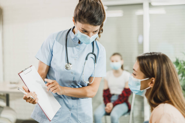 Enfermera hablando con una mujer joven antes de la vacuna covid-19 en la sala de espera del hospital. - Foto, Imagen