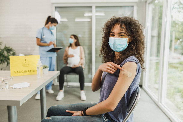 Een Afro-Amerikaans tienermeisje dat met een pleister aan haar arm te zien is na toediening van het Covid-19 vaccin. - Foto, afbeelding