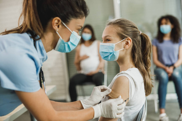 Een verpleegster die een pleister aanbrengt bij een schattig tienermeisje na toediening van het Covid-19 vaccin. - Foto, afbeelding