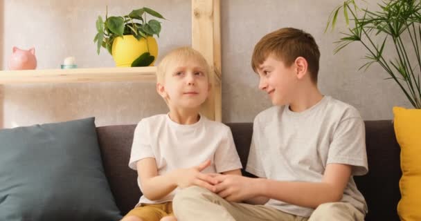 Dois meninos alegres se comunicam sentados em casa no sofá. Amizade e fraternidade. Vista frontal da luz do dia - Filmagem, Vídeo