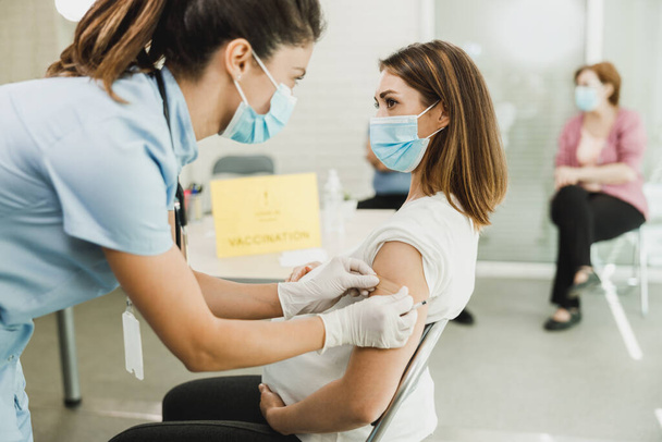 コロナウイルスの流行によりワクチンを接種した後、若い妊婦へのバンドエイドを適用する看護師. - 写真・画像