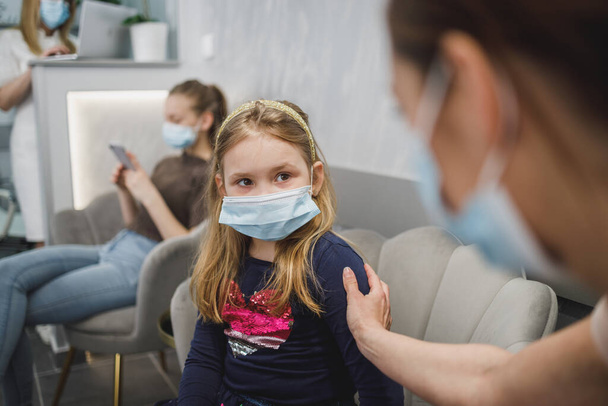 Worried little girl and her mom with face mask in waiting room at dentist's office. - Foto, immagini