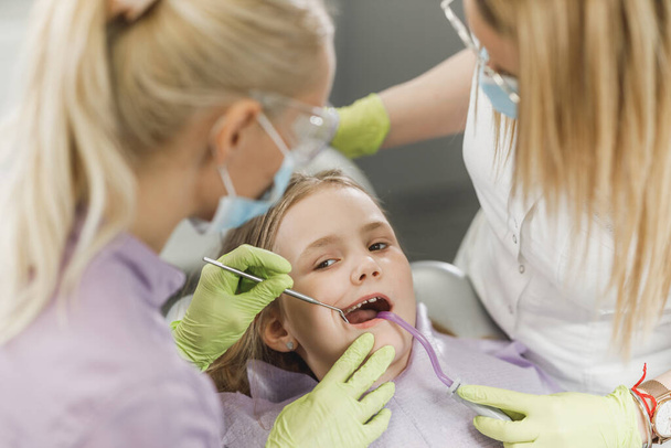 Urocza dziewczynka poddana badaniu zębów przez dentystę w klinice dentystycznej. - Zdjęcie, obraz