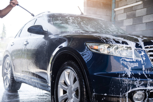 Der Mann wäscht den Schaum mit dem Wasserdruck aus dem Auto - Foto, Bild