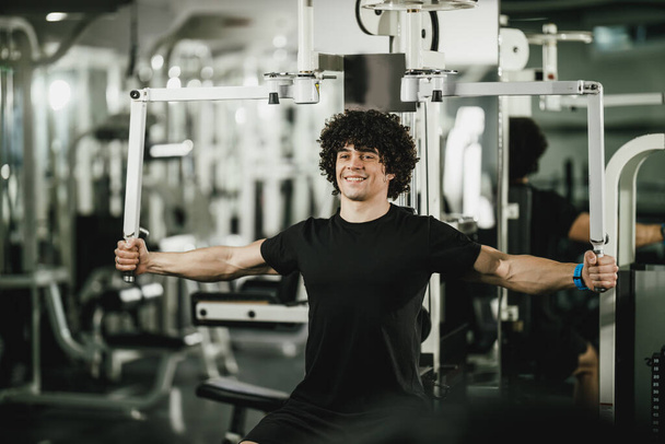Un jeune homme musclé s'entraîne sur une machine dans la salle de gym. - Photo, image