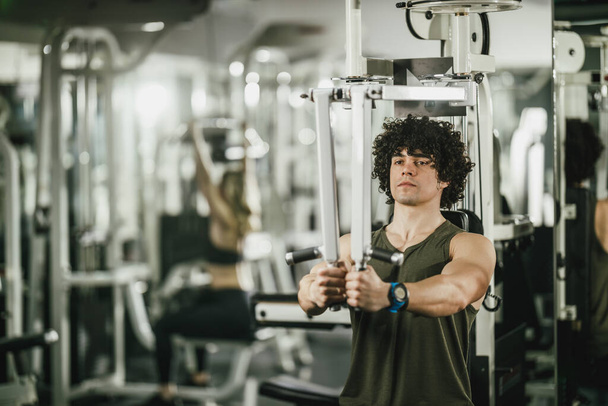 Ein junger muskulöser Mann trainiert im Fitnessstudio an einem Gerät. - Foto, Bild