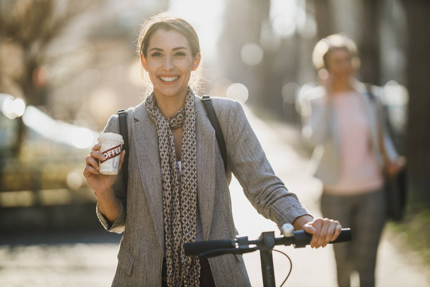 Молода бізнес-леді п'є каву під час переходу на роботу з електричним скутером
. - Фото, зображення