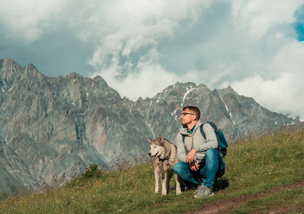 Ελκυστικός σπορ άνθρωπος με husky μαζί απολαμβάνοντας ορεινό τοπίο - Φωτογραφία, εικόνα