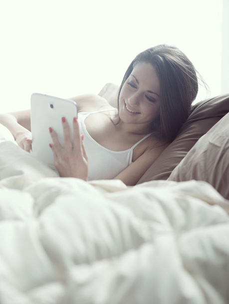 Woman enjoying with a digital tablet in bed in the morning - Foto, afbeelding