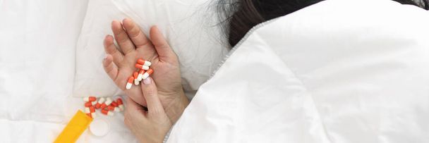 Womans hand sticks out from under blanket, pills lie on her hand. - Foto, afbeelding