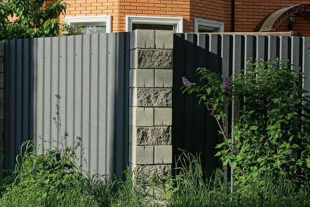 mur ogrodzeniowy z szarego żelaza i cegieł porośniętych zieloną roślinnością i trawą - Zdjęcie, obraz