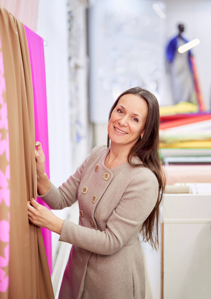 Vrouwelijke lachende ontwerper kiezen bruine en roze stoffen - Foto, afbeelding