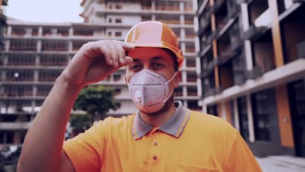 Foreman in protective helmet and respirator checking the construction process and talking with a worker looking at the camera at a construction site against the background of a building building - Záběry, video