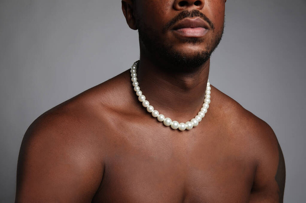 Cropped image of shirtless black man with pearl necklace over grey background. - Фото, зображення