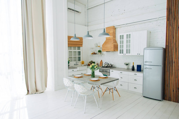 Minimal cozy light home style, scandinavian interior. White furniture with utensils, shelves with crockery and plants in pots, refrigerator in simple dining room, panorama, empty space - Photo, Image