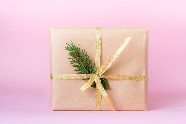 Gift box with a decor of branches of a Christmas tree and a gold ribbon on a pink paper background. copy space. Recycled paper used. - Photo, image
