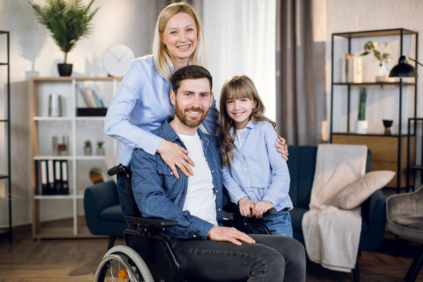 Man sitting in wheelchair while wife and daughter hug him - Zdjęcie, obraz