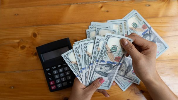 Eine Handvoll amerikanischer Dollar fließt in menschliche Hände. Geschäft und Bargeld mit Taschenrechner auf dem Tisch - Foto, Bild