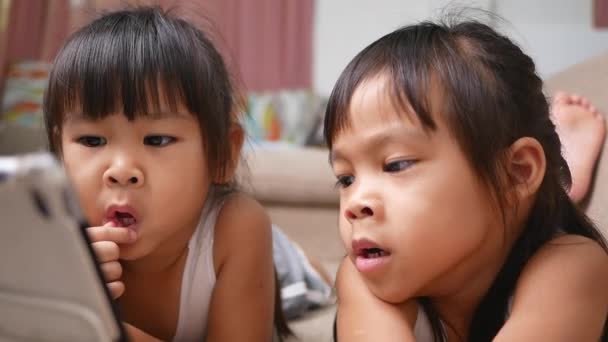 Két testvér lány fekszik a kanapén, és digitális tableteket néznek együtt a nappaliban.. - Felvétel, videó