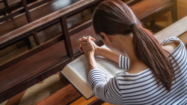 Christian woman praying on holy bible in the public church. Woman pray for god blessing to wishing have a better life and believe in goodness. - Photo, image