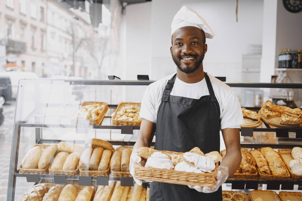 African American baker holding tray of bread in bakery - Foto, Imagen