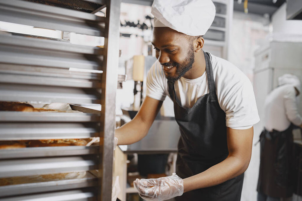 African American baker in uniform sorting baked products on pallets - Foto, imagen