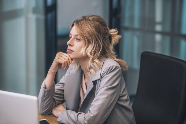 Young adult woman in suit sitting at workplace - Photo, Image