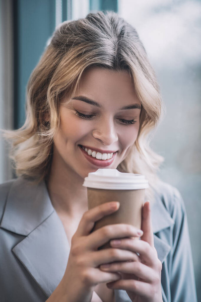Smiling woman with drooping eyelids bringing coffee to face - Фото, зображення