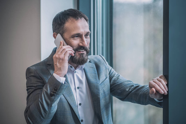 Successful man in suit talking positively on smartphone - Fotoğraf, Görsel